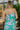 Upper back view of model wearing the Wanderlust Floral Midi Dress that has green, lavender and orange fabric with a floral pattern, midi length, a square neckline,  and adjustable straps.