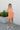 Full body front view of model wearing the Good Vibes Romper that has coral gauze fabric, pockets on each side, a square neckline, straps, an open back, and an elastic waistband.
