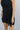 Close front view of model wearing the On Your Mind Dress that has black fabric with black lining, a one-shoulder neckline, a sleeveless design, a wrap skirt overlay with a side tie, and a back zipper with a hook closure.