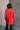 Back view of model wearing the Julianna Red Satin Long Sleeve Top that has red satin fabric, a high-low hem, a chest pocket, a notched collar neck, and long sleeves with buttoned cuffs.