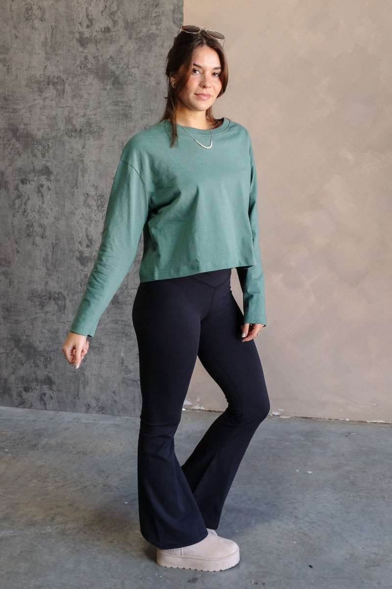 Full body side view of model wearing the Nicole Green Cropped Long Sleeve Sweatshirt that has gray-green cotton fabric, a cropped waist, a round neckline and long sleeves.