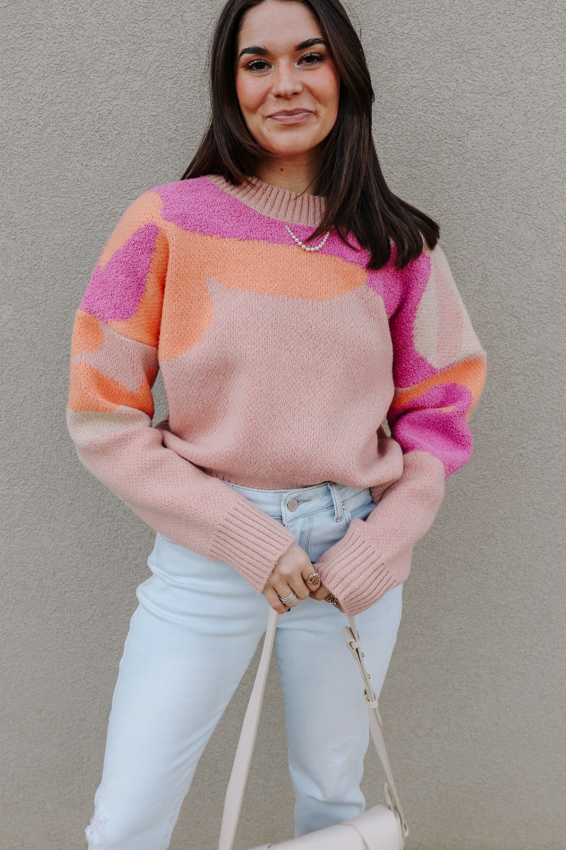 Front view of model wearing the Mila Pink Multi Long Sleeve Sweater which features orange, peach, cream and fuschia knit fabric, an upper floral print, ribbed hem, a ribbed round neckline, dropped shoulders, and long sleeves with ribbed cuffs.