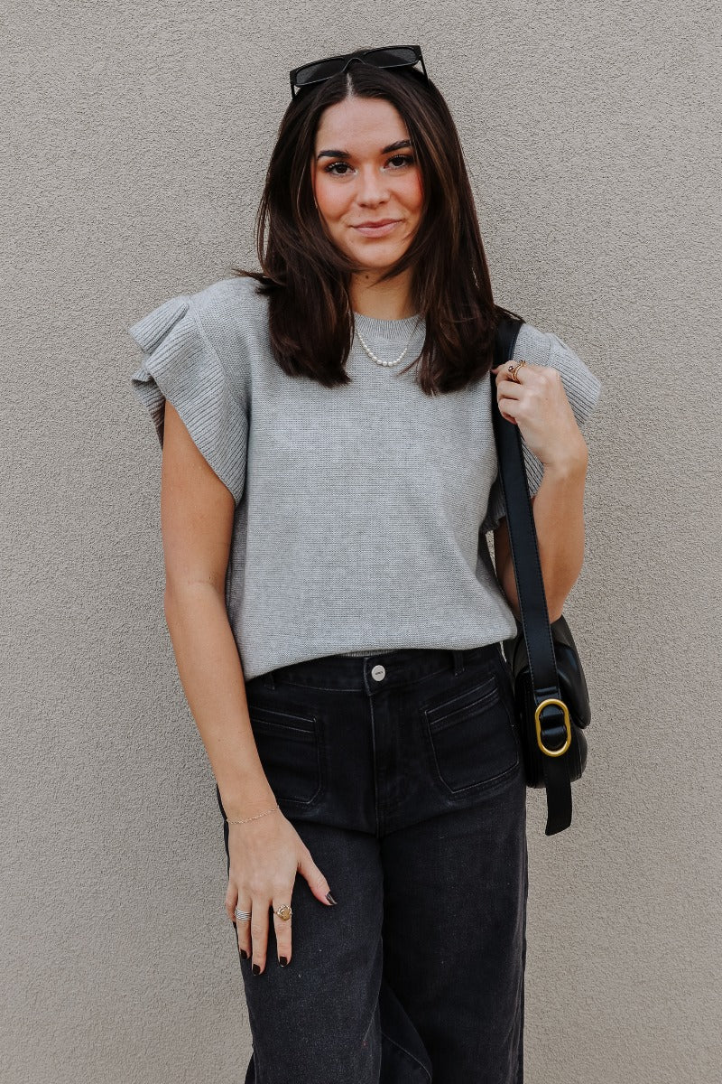 Front view of model wearing the Sierra Heather Grey Knit Ruffle Sweater which features heather grey knit fabric, ribbed hem, a round neckline, and short sleeves with ruffle details.