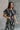 Front view of model wearing the Genevieve Black & Cream Printed Short Sleeve Top that has black fabric with a cream aztec pattern, a cropped waist, bubble hem, round neckline, a back key hole with a button, and short sleeves.