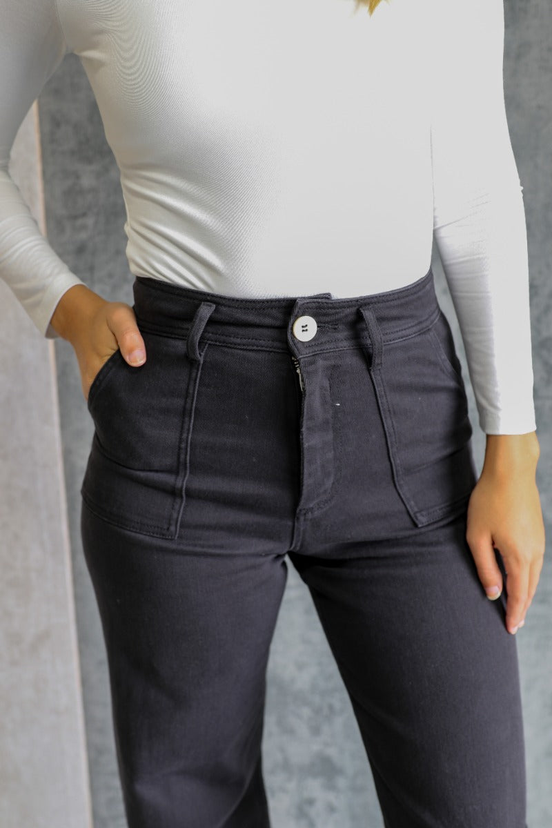 Close up view of model wearing the Alexa Black High-Waisted Wide Leg Pants which features black denim fabric, two front pockets, two back pockets, front zipper with button closure, belt loops and wide pant legs.