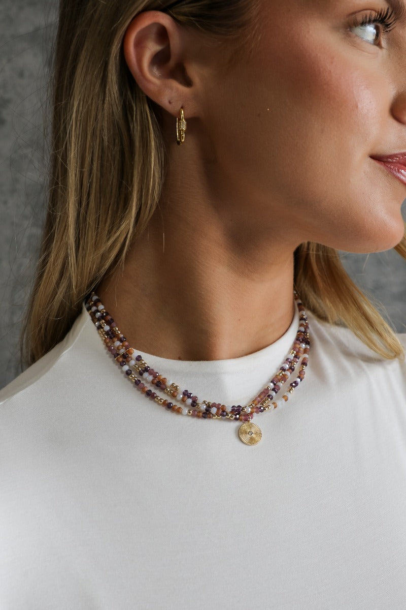 front view of model wearing the Penelope Beaded Layered Necklace that features three attached strands with brown, gold, and white beading and a circular gold charm.