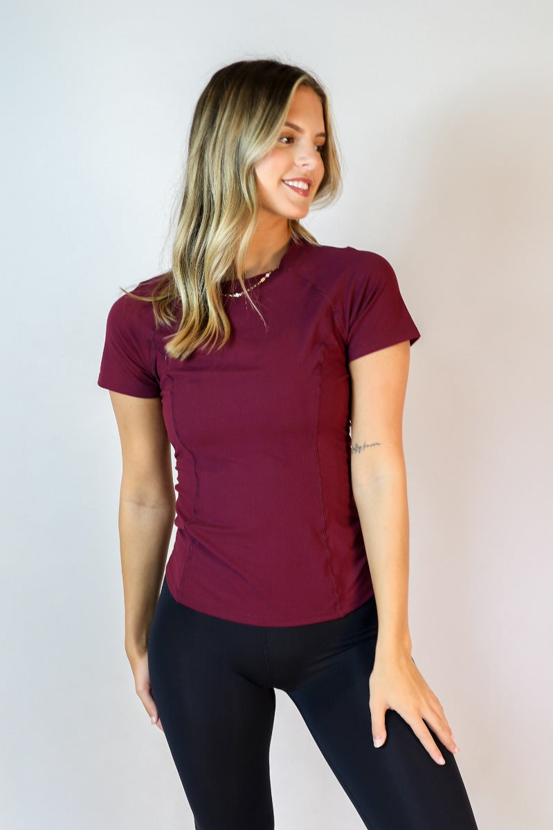 Front view of model wearing the Robin Burgundy Athletic Short Sleeve Top which features burgundy athleisure fabric, monochrome stitch details, a scooped neckline, and short sleeves.