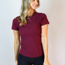 Front view of model wearing the Robin Burgundy Athletic Short Sleeve Top which features burgundy athleisure fabric, monochrome stitch details, a scooped neckline, and short sleeves.