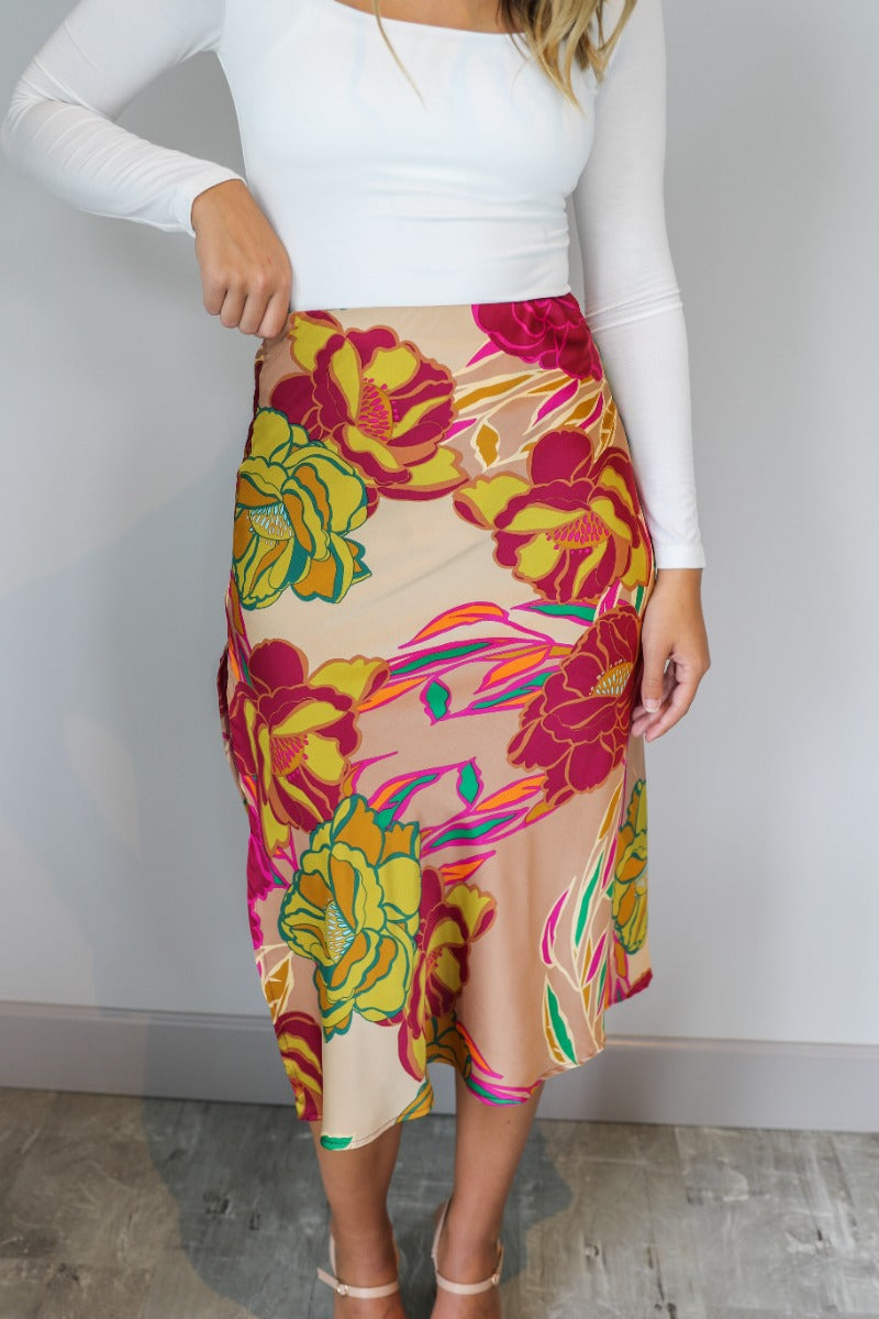 Close front view of model wearing the Lilianna Floral Satin Midi Skirt that has taupe satin fabric with a floral print, midi length, a slit on the back, and an elastic waistband.