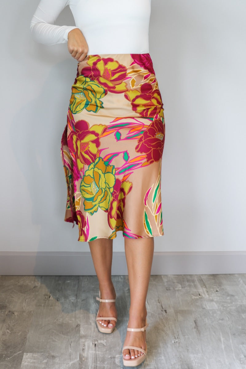Front view of model wearing the Lilianna Floral Satin Midi Skirt that has taupe satin fabric with a floral print, midi length, a slit on the back, and an elastic waistband.