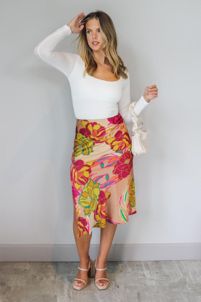 Front view of model wearing the Lilianna Floral Satin Midi Skirt that has taupe satin fabric with a floral print, midi length, a slit on the back, and an elastic waistband.