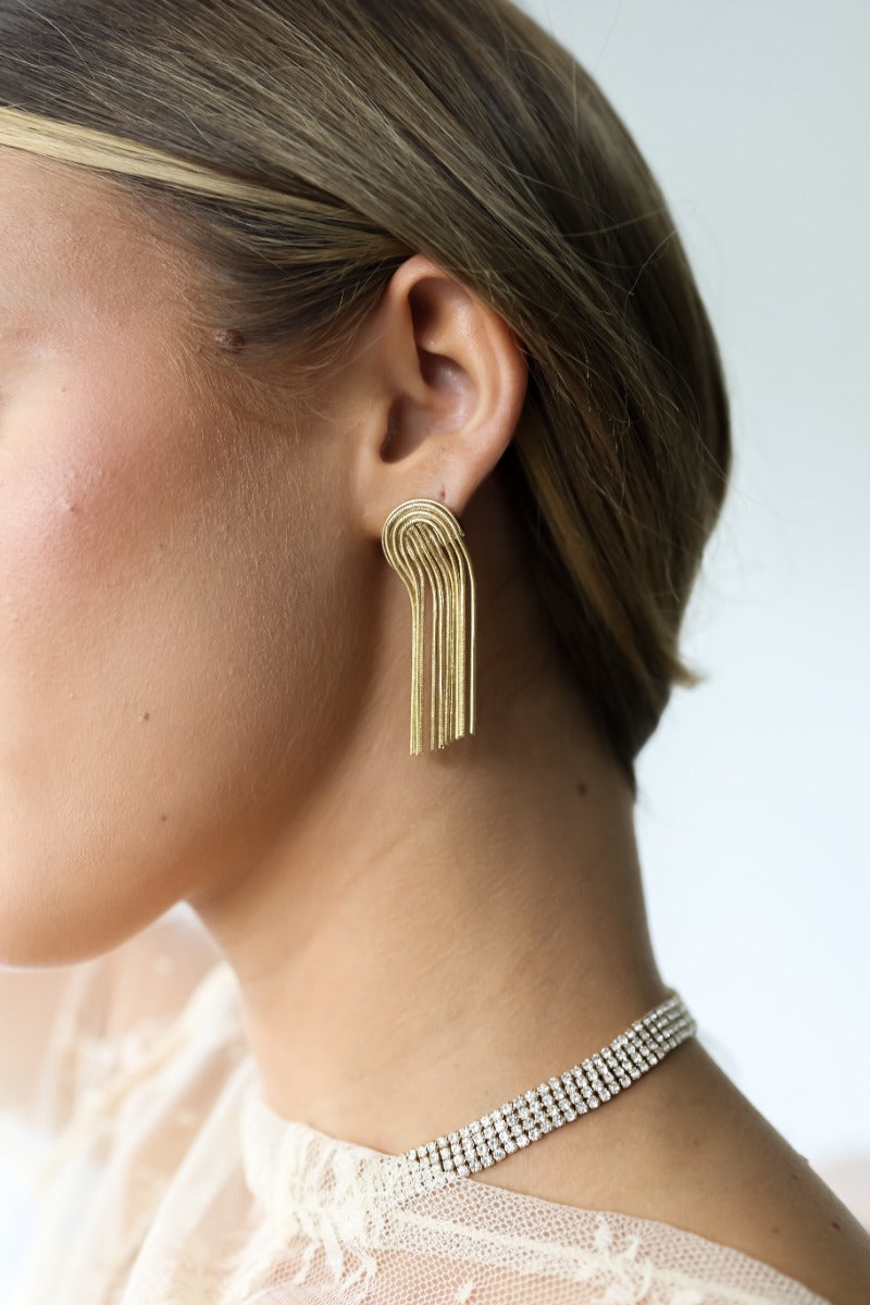 Side view of model wearing the Celine Gold Arch Fringe Earrings that feature gold arches on post backs with gold fringe.