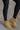 Frontal side view of model wearing the Oamira Beige Suede Platform Booties that have camel suede uppers with beige faux-fur lining and 2 inch platform soles.