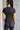 Back view of model wearing the Robin Black Athletic Short Sleeve Top that has black athleisure fabric, monochrome stitch details, a scooped neckline, and short sleeves.