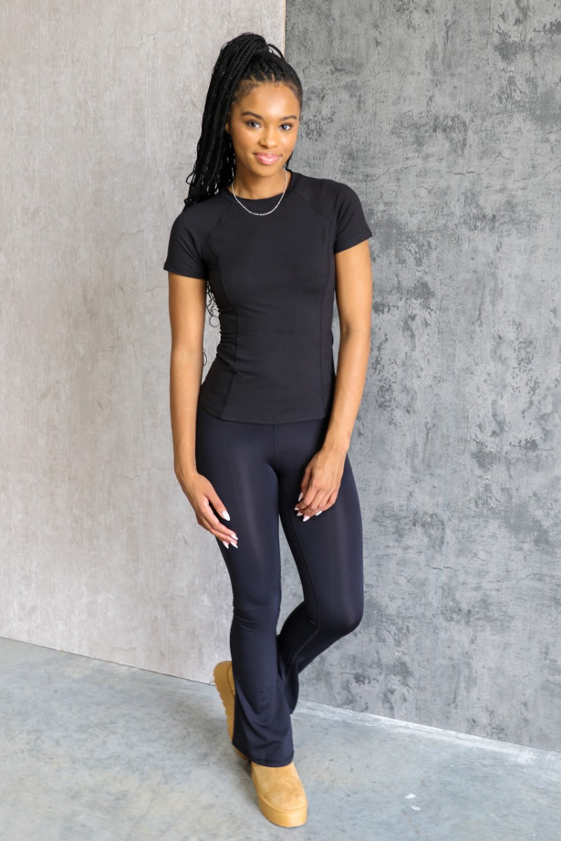 Full body front view of model wearing the Robin Black Athletic Short Sleeve Top that has black athleisure fabric, monochrome stitch details, a scooped neckline, and short sleeves.