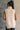 Back view of model wearing the Olivia Beige Cable Knit Turtleneck Sleeveless Sweater which features beige cable knit fabric, high low hem, turtleneck neckline and sleeveless.
