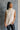 Front view of model wearing the Olivia Beige Cable Knit Turtleneck Sleeveless Sweater which features beige cable knit fabric, high low hem, turtleneck neckline and sleeveless.