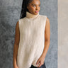 Front view of model wearing the Olivia Beige Cable Knit Turtleneck Sleeveless Sweater which features beige cable knit fabric, high low hem, turtleneck neckline and sleeveless.