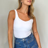 Front view of model wearing the Avery White Sleeveless Bodysuit which features white knit fabric, a scooped neckline, thick straps, and a thong bottom with snap closures.