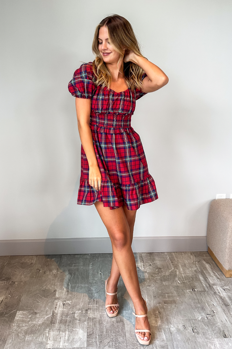 Full body view of model wearing the Phoebe Red Multi Check Short Puff Sleeve Mini Dress which features red, blue, green, yellow and white knit fabric, plaid pattern, mini length, flared skirt hem, smocked waist with ruffles detail, scooped neckline and sh