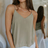 Front view of model wearing the Smooth Talker Tank Top that has dark sage fabric with a lining, a v-neckline, and spaghetti straps.
