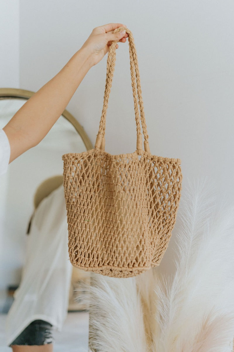 Front view of model holding the Resort Ready Purse which features straw material and camel coloring, lined pocket on the inside with drawstring closure and braided straps.