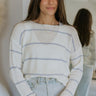 Front view of model wearing the Rainy Day Striped Top that has white knit fabric with a light blue stripe pattern, a high-low hem, a round neck, dropped shoulders, and long sleeves