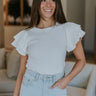 Front view of model wearing the Out Of Your League Top that has ribbed off white fabric, a round neckline, and short sleeves with ruffle details.