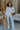 Full body front view of model wearing the Simply Yours Top that has ivory fabric with tan stitched stripes, a high-low hem, a notched neck with a tie and 3/4 sleeves