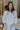 Front view of model wearing the Simply Yours Top that has ivory fabric with tan stitched stripes, a high-low hem, a notched neck with a tie and 3/4 sleeves