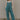Full body front view of model wearing the Ready To Road Trip Jumpsuit that has washed blue fabric, a v-neck, distressing, two side pockets, thin straps, and wide pants legs with elastic hems.