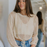 Front view of model wearing the Coastal Sands Top that has natural loose-knit fabric, a drawstring hem with a tie, a round neckline, and long flared sleeves.