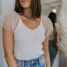 Close up view of model wearing the Falling For You Ruffle Top which features off white ribbed fabric, a v neckline, and a sleeveless body with sheer ruffle details.