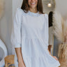 Front view of model wearing the All My Love Dress that has white knit fabric, a mini-length hem, a baby doll style with a tiered skirt, a round neckline, and puff sleeves