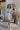 Full body view of model wearing the Enchanted Times Dress which features light blue and light purple fabric with purple embroidered flowers, a lining, a mini-length hem, a cutout in the mid section, a plunge neckline, a back zipper, and sheer balloon slee