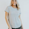 Front view of model wearing the Simply Made Top in Grey features heather grey knit fabric, a round neckline, a scooped hem, and short sleeves with folded cuffs.