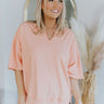 Front view of model wearing the Sunrise Views Top which features light peach fabric, a high-low hem with side slits, a notched neckline, dropped shoulders, and short sleeves.