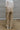 Close up/ back view of model wearing the Nothing On You Pants which features taupe nylon fabric, front buttoned pockets, back buttoned pockets, an elastic waistband with drawstring ties, and wide legs with drawstring hems.
