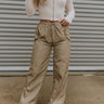 Front view of model wearing the Nothing On You Pants which features taupe nylon fabric, front buttoned pockets, back buttoned pockets, an elastic waistband with drawstring ties, and wide legs with drawstring hems.