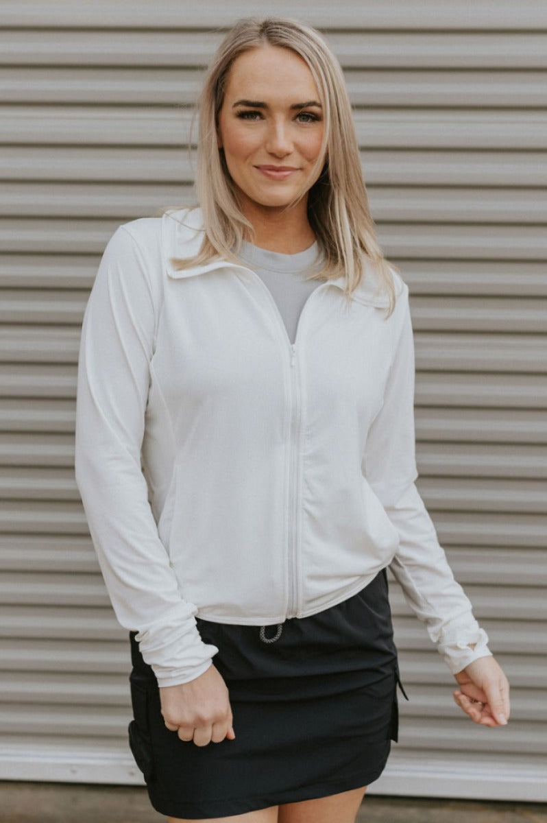 Front view of model wearing the All I Want Lightweight Jacket features white fabric, a monochromatic zip up, two front pockets, a high neckline with drawstrings and a hood, an elastic hem, a lining in the front, and long sleeves with cuffs.