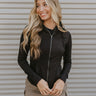 Front view of model wearing the Working It Jacket in Black which features black athleisure fabric, a monochromatic zip up, two front pockets, a high neckline with drawstrings and a hoodie attached, a lining, and long sleeves.