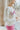 Side view of model wearing the Crazy In Love Sweater that has white knit fabric with a distressed hem, a round neckline,and  long sleeves The sweater says "Crazy in Love" in pink frill fabric