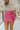Front view of model wearing the Always On My Mind Skort that has pink fabric, a skirt overlay with shorts in the back, a front bow detail, a pink lining, and a monochromatic side zipper with a hook closure