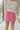 Back view of model wearing the Always On My Mind Skort that has pink fabric, a skirt overlay with shorts in the back, a front bow detail, a pink lining, and a monochromatic side zipper with a hook closure