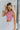 Side view of model wearing the Crushing On You Top which features pink bubble fabric, a cropped waist, a round neckline, a back keyhole with button a closure, and a sleeveless body.