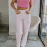 Front view of model wearing the Between You and Me Pants which features light pink denim fabric, two front pockets, two cargo side pockets, a front zipper and button closure, belt loops, two cargo back pockets, and wide legs.
