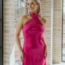Front view of model wearing the Midnight Hour Dress which features fuchsia satin fabric, a mini-length hem, a halter neck with a back tie, an open back and sleeveless body.