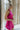 Side view of model wearing the Midnight Hour Dress which features fuchsia satin fabric, a mini-length hem, a halter neck with a back tie, an open back and sleeveless body.