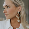 Side view of model wearing the Enchanted Dreams Earrings which features ivory diamond shaped pattern with a ball attachment which has gold thread, cream yarn and flowers.