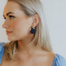 Side view of model wearing the Midnight Dreams Earrings which features blue carved stone with gold details.